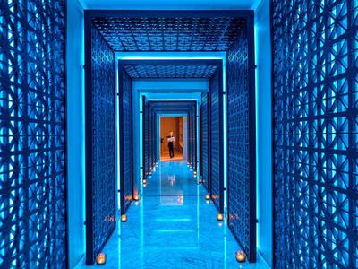 Blue modern hotel corridor with illuminated walls and candles along the floor.