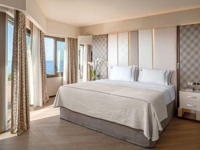 Modernes Hotelzimmer mit großem Bett, Meerblick und hellem, elegantem Interieur.