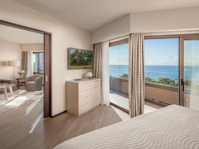 Helles Hotelzimmer mit Meerblick, hellen Holzmöbeln und Zugang zu Balkon.