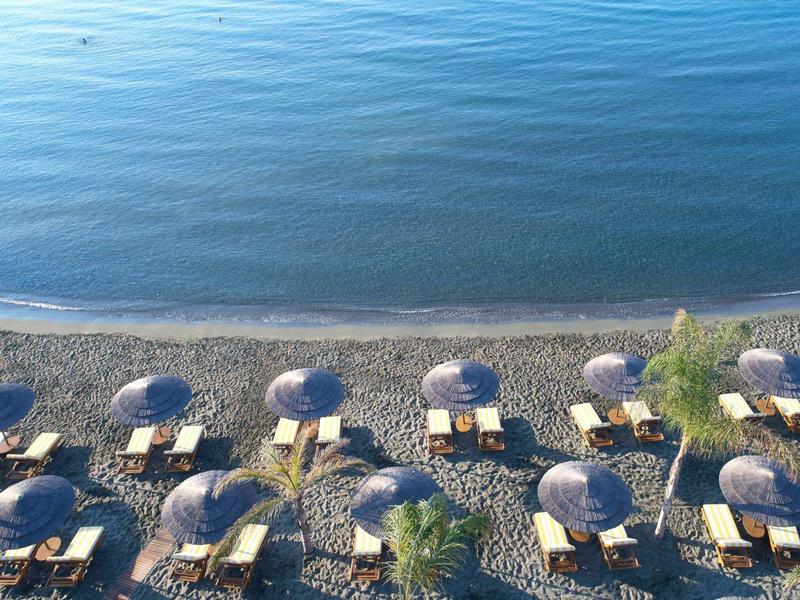 Beach with umbrellas and sun loungers beside calm, blue water.