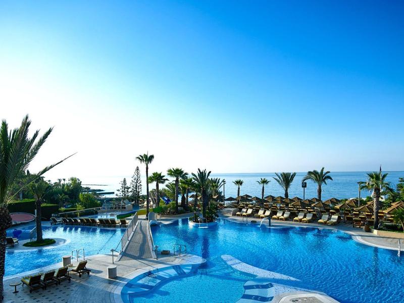View of a tropical hotel pool with lounge chairs and palm trees by the sea