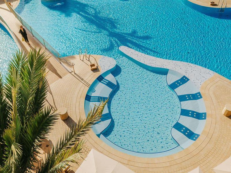 Shaped pool with seating area and palm trees in sunny hotel setting.