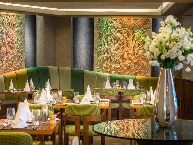 Elegant restaurant with green chairs, artistic wall reliefs, and decorative flowers in a vase.