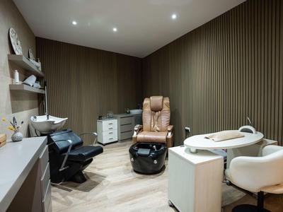 Modernes Kosmetikstudio mit braunen Wänden, Ledersessel, Waschbecken und verschiedenen Arbeitsstationen.