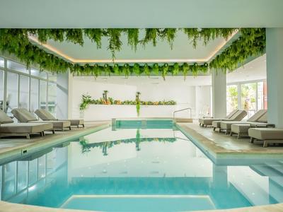 Moderner Innenpool mit Liegestühlen, grünen Pflanzen an der Decke und natürlichem Licht.