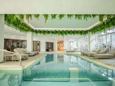 Espace piscine intérieure moderne avec plantes suspendues et chaises longues dans un hôtel.