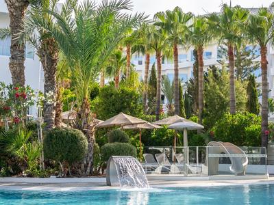 Espace piscine avec parasols et chaises longues, entouré de palmiers et de verdure.