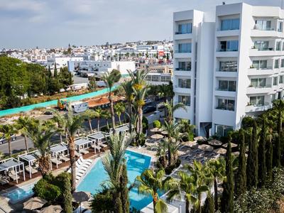 Moderner Hotelkomplex mit Pool, Palmen und weißen mehrstöckigen Gebäuden unter blauem Himmel.