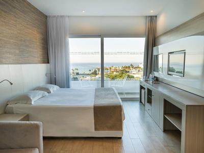 Helles Hotelzimmer mit Doppelbett, großem Fenster, Meerblick und modernem Holzmobiliar.