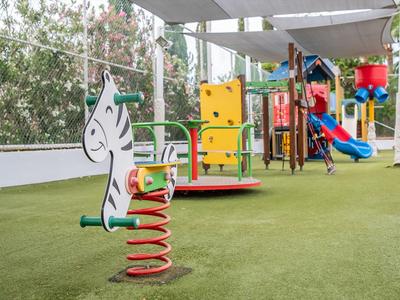 Bunter Spielplatz mit Feder-Schaukel, Klettergerüst und Rutsche auf grünem Kunstrasen.