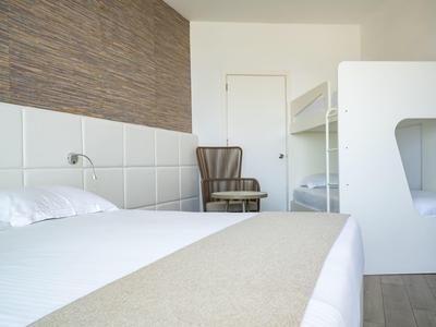 Helles Zimmer mit Doppelbett, Etagenbett, gestreiftem Sessel und Holzwandakzent.