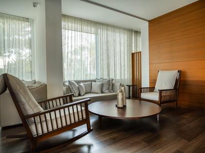 Salon moderne avec chaises en bois, table ronde et grandes fenêtres avec rideaux.