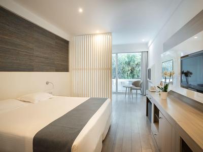 Modernes Schlafzimmer mit großem Bett, Holzverkleidung, TV an Wand und Zugang zu Balkon mit Pflanzen.