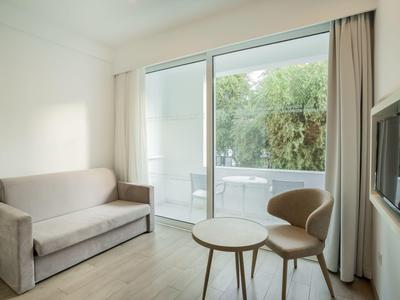 Modernes Wohnzimmer mit grauem Sofa, zwei kleinen Tischen, Stuhl und großer Glas-Schiebetür zum Balkon.