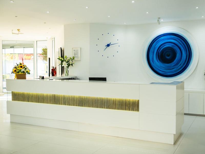 Helle, moderne Rezeption mit weißem Tresen, blauem Wandbild und Blumenarrangements.