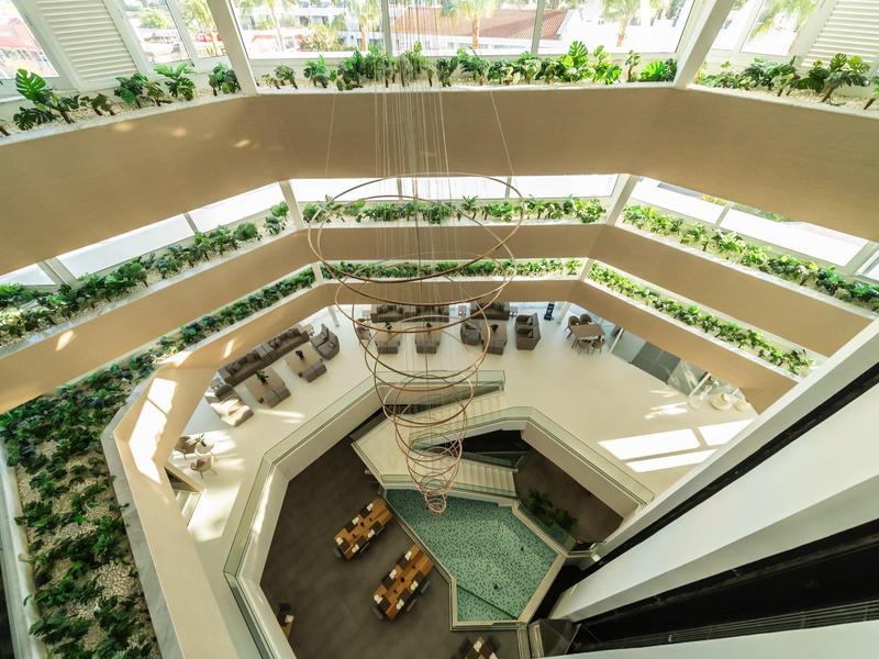 Innenansicht eines modernen Gebäudes mit drei begrünten Etagen und Tischen im Atrium.