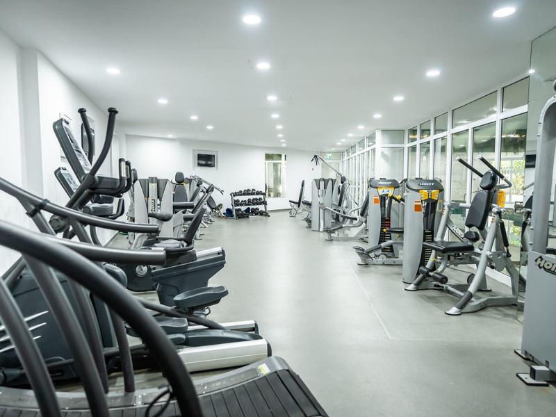 Moderne, helle Fitnessstudio mit verschiedenen Cardiogeräten und Kraftmaschinen in reihiger Anordnung.