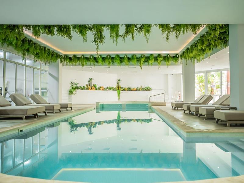 Moderner Innenpool mit Liegestühlen, grünen Pflanzen an der Decke und natürlichem Licht.