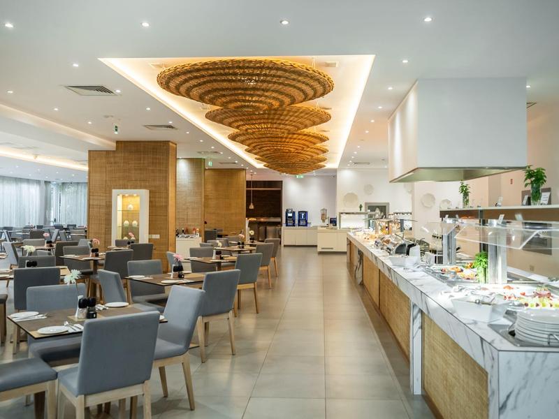 Modernes Restaurant mit grauen Stühlen, Holztischen und Buffetbereich unter heller Deckenbeleuchtung.