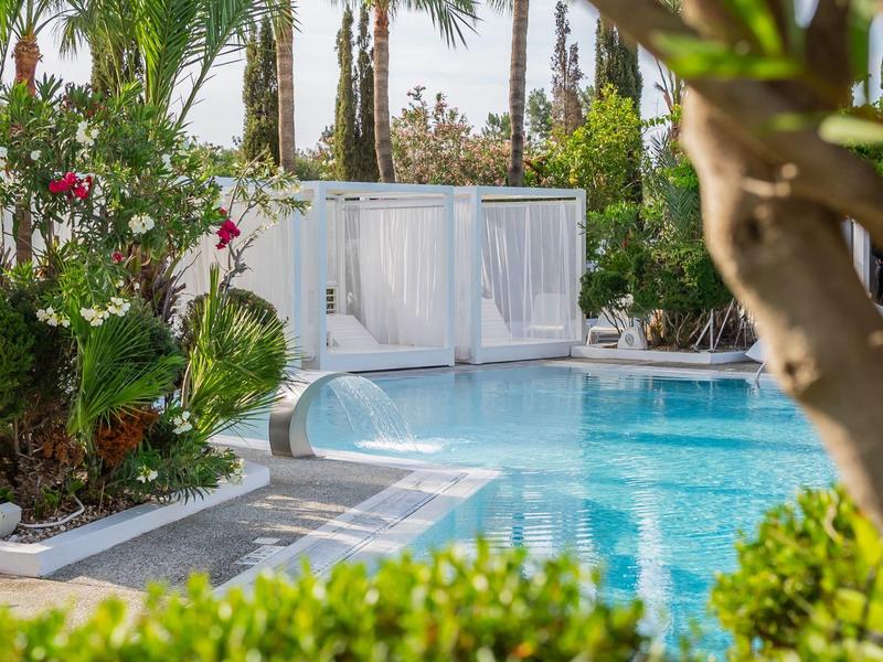 Schwimmbad mit klarem Wasser, umgeben von grünen Pflanzen und weißen Vorhängen an einer Lounge.