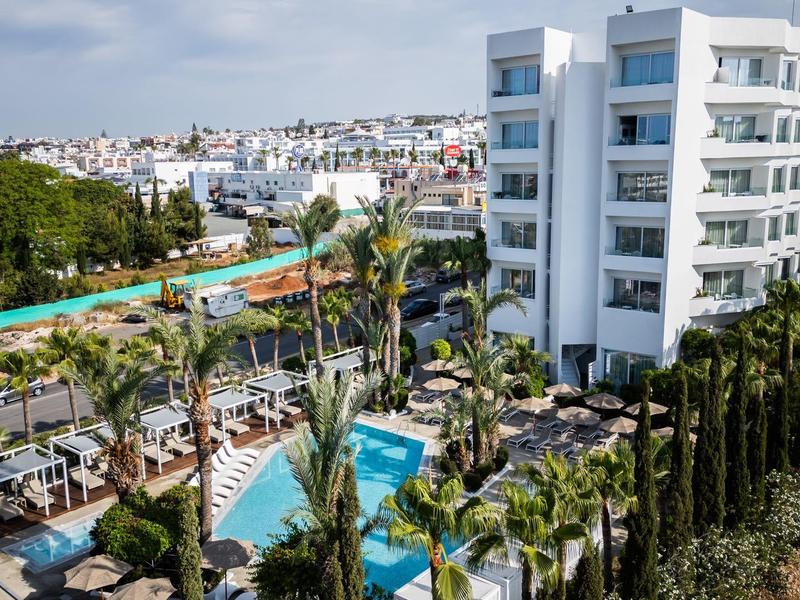 Moderner Hotelkomplex mit Pool, Palmen und weißen mehrstöckigen Gebäuden unter blauem Himmel.