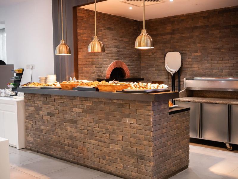 Moderne Theke mit Holzoptik, Backofen und frischem Gebäck unter drei Hängelampen.