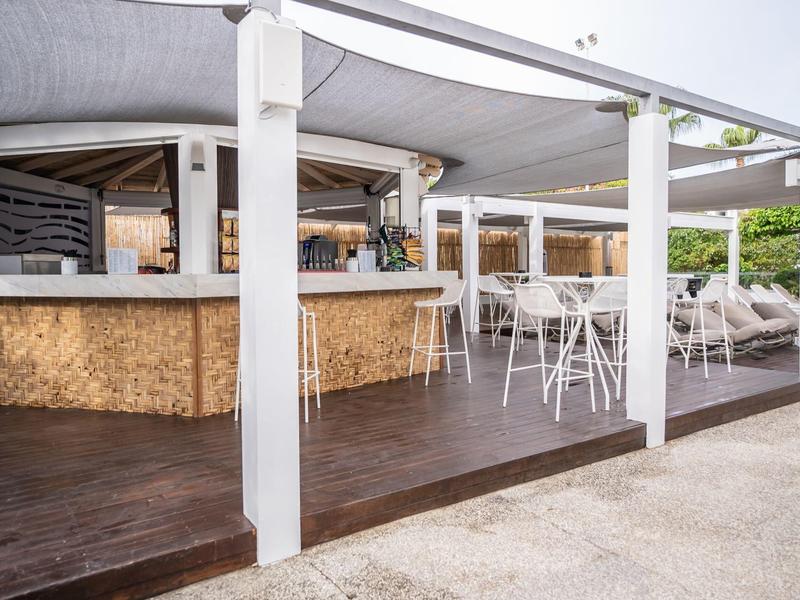 Offene Terrasse mit weißen Stühlen, hohem Holztresen und dunkelbraunem Holzboden.