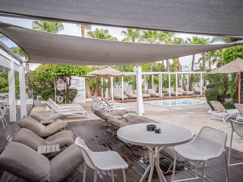 Moderne Terrasse mit Sitzgruppen, schattenspendenden Segeln und einem Swimmingpool im Hintergrund.