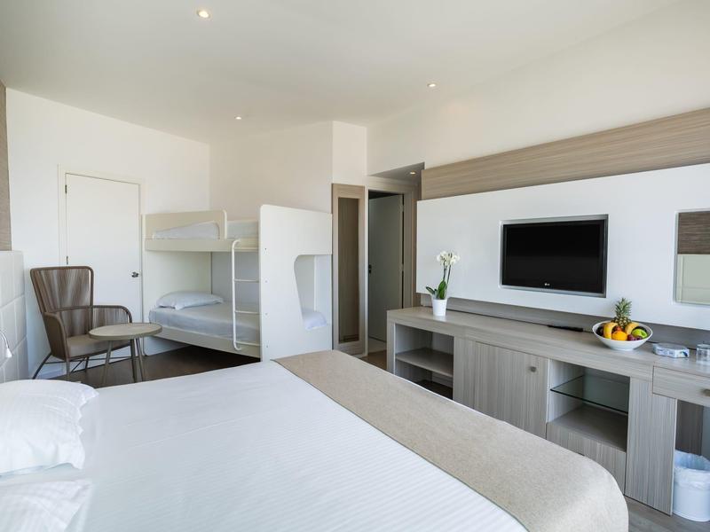 Helles Schlafzimmer mit Doppelbett, Etagenbett, TV, Sesseln und modernem Schrank in neutralen Tönen.