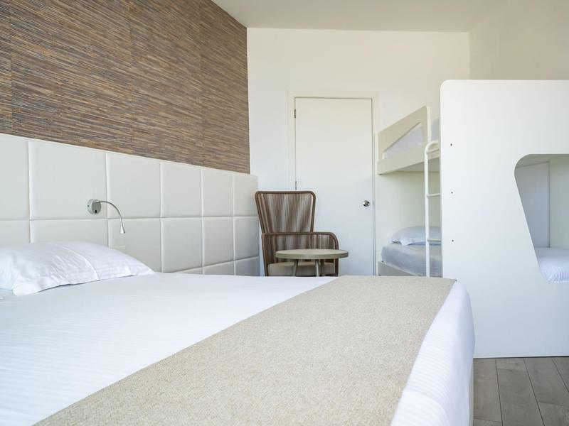 Helles Zimmer mit Doppelbett, Etagenbett, gestreiftem Sessel und Holzwandakzent.