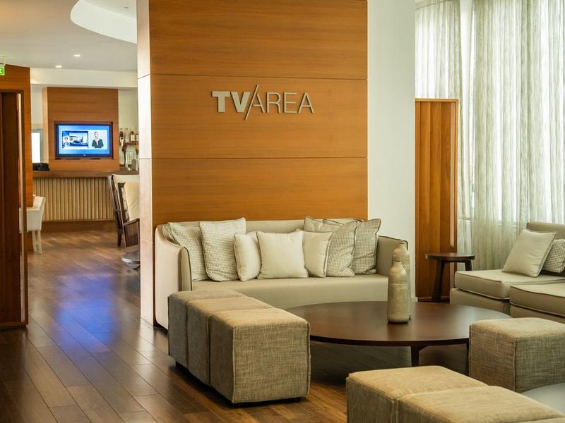 Gemütlicher Warteraum mit beigen Sofas, Holzwänden und Tageslicht durch Vorhänge.