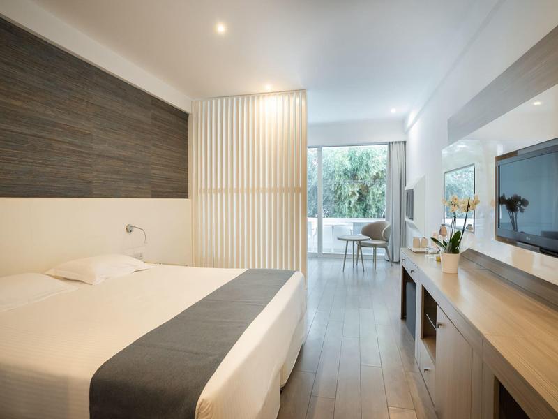 Modernes Schlafzimmer mit großem Bett, Holzverkleidung, TV an Wand und Zugang zu Balkon mit Pflanzen.