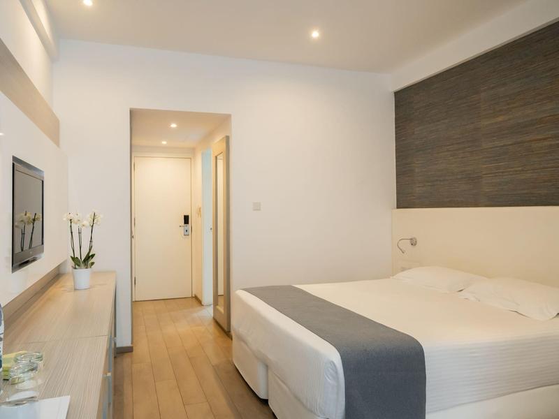 Kleines modernes Hotelzimmer mit Doppelbett, Holzfußboden und schlichtem weiß-grauem Design.