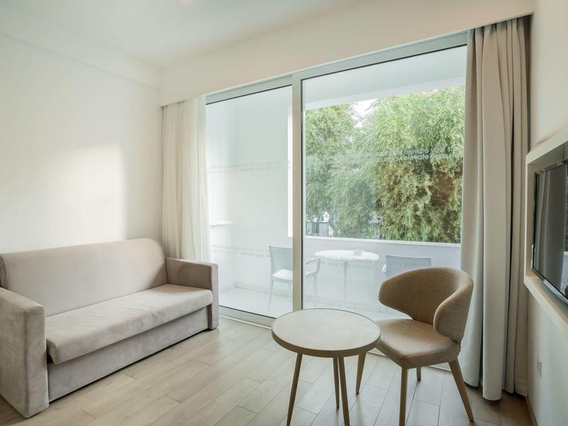 Modernes Wohnzimmer mit grauem Sofa, zwei kleinen Tischen, Stuhl und großer Glas-Schiebetür zum Balkon.