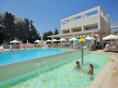 Hotel z dużym basenem, parasolami i dwoma osobami w brodziku w słoneczny dzień.