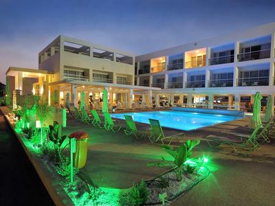 Modernes Hotel mit beleuchtetem Pool und grüner Gartenbeleuchtung bei Dämmerung.