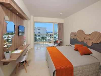 Nowoczesny pokój hotelowy z łóżkiem podwójnym, pomarańczowymi akcentami i widokiem na basen i morze.