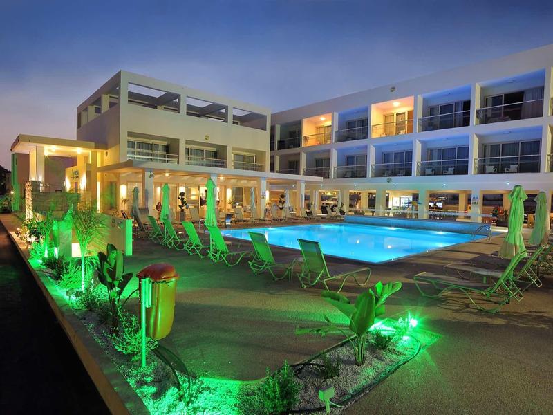 Modernes Hotel mit beleuchtetem Pool und grüner Gartenbeleuchtung bei Dämmerung.