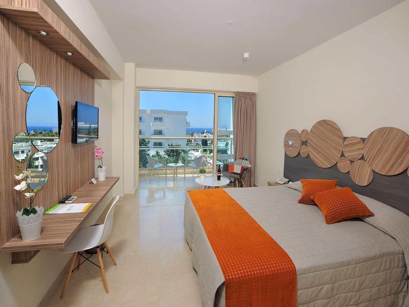 Modernes Hotelzimmer mit Doppelbett, orangefarbener Decke und Kissen, Holzdekoration und Balkonblick.