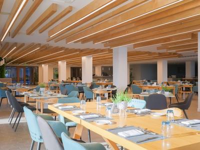 Restaurante moderno con techo de vigas de madera y sillas azul grisáceo en mesas de madera clara.