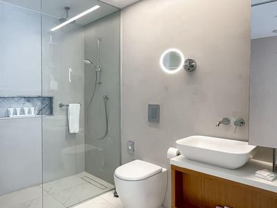 Modernes Badezimmer mit Glasdusche, Wandtoilette, integriertem Waschbecken und großen weißen Fliesen.