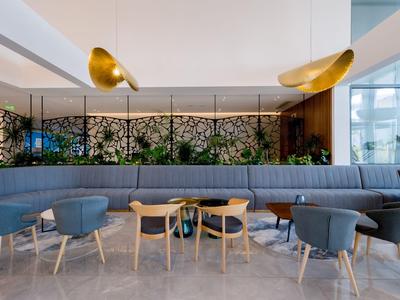 Área de descanso moderna con sillas azules y sofá largo en interior luminoso de hotel.