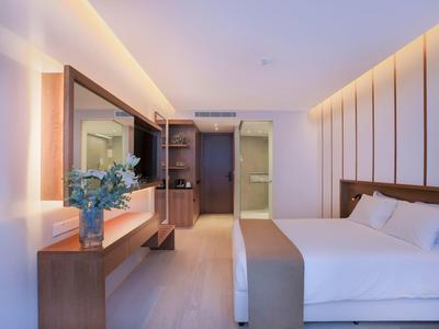 Modernes Hotelzimmer mit großem Bett, Holzverkleidung, beleuchtetem Spiegel und Blume auf dem Tisch.