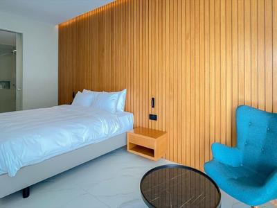 Modernes Schlafzimmer mit Holzpaneelwand, Doppelbett, blauem Sessel und rundem Glastisch.