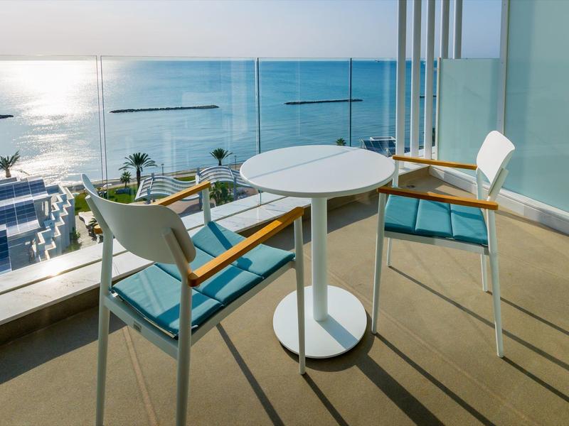 Balkon mit weißem Tisch, zwei Stühlen und Meerblick bei Sonnenlicht am späten Nachmittag.