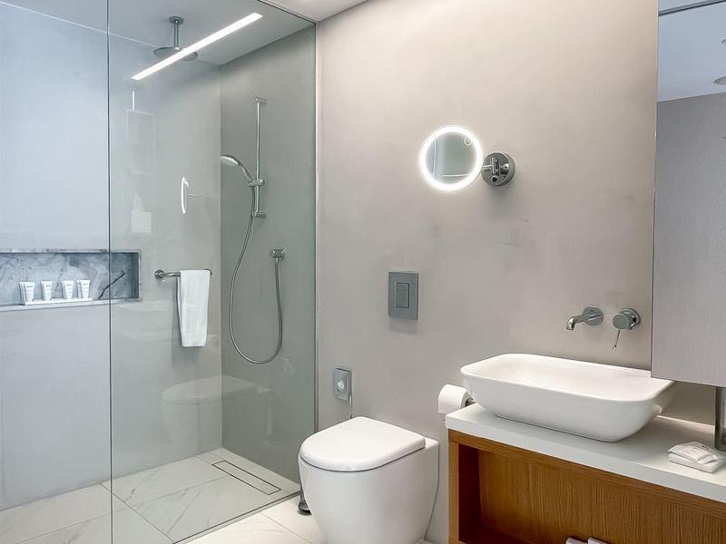 Modernes Badezimmer mit Glasdusche, Wandtoilette, integriertem Waschbecken und großen weißen Fliesen.