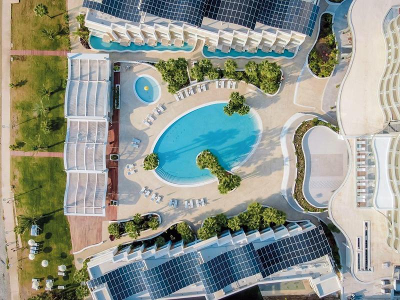 Moderne Hotelanlage mit ovalem Pool, umgeben von Liegestühlen und angrenzendem Strand.