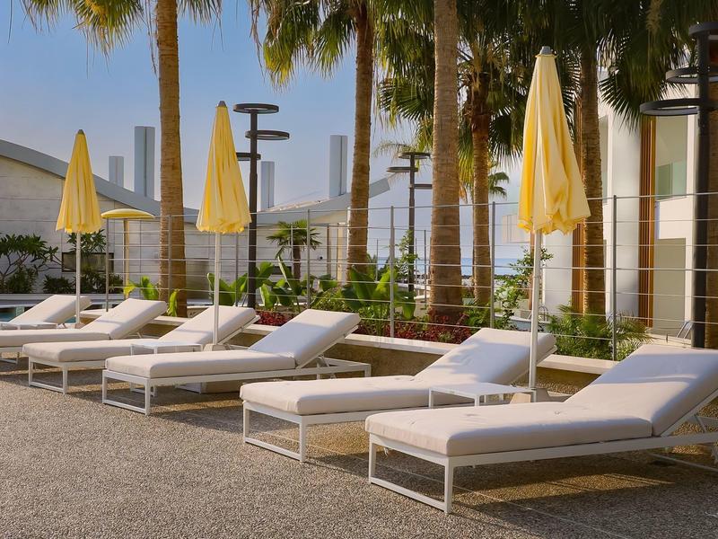 Mehrere weiße Liegestühle mit gelben Sonnenschirmen stehen nebeneinander an sonnigem Poolbereich.