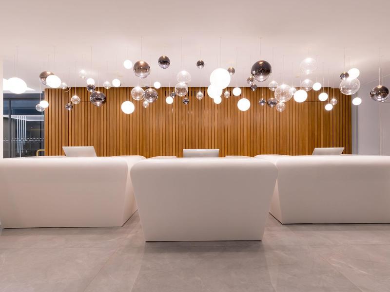 Moderner Warteraum mit weißen Sofas und hängenden Kugelleuchten vor einer Holzpaneelwand.