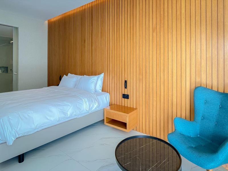 Modernes Schlafzimmer mit Holzpaneelwand, Doppelbett, blauem Sessel und rundem Glastisch.